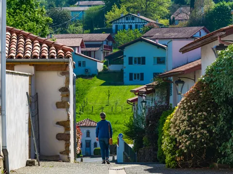 Persona caminando entre casas blancas y verdes prados en Ainhoa, en el País Vasco francés.