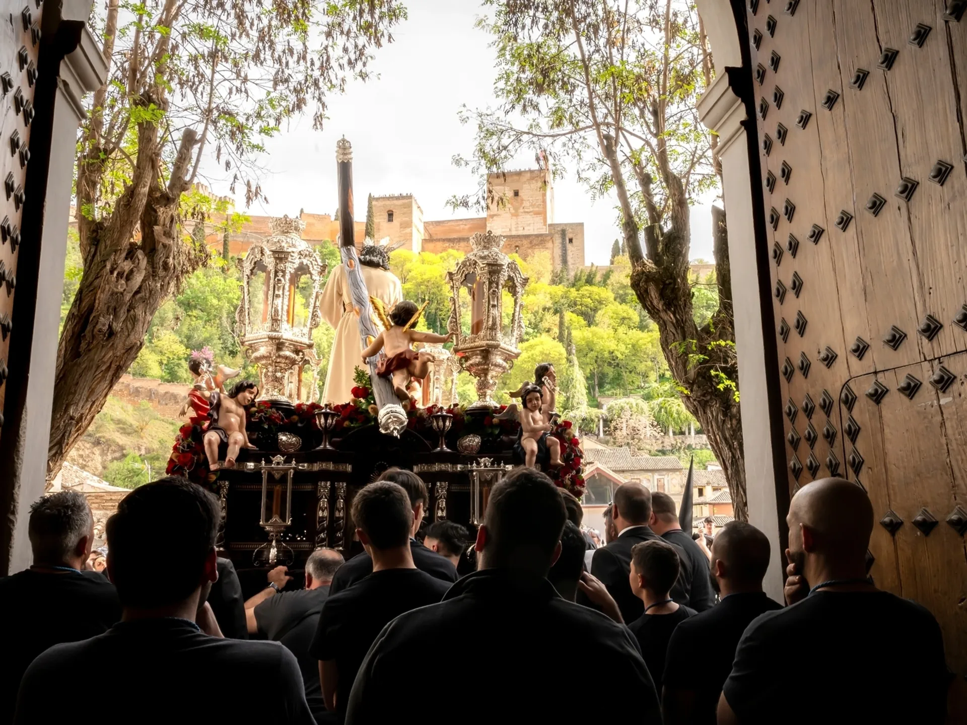 Paso de Semana Santa saliendo de iglesia con la Alhambra de Granada al fondo.