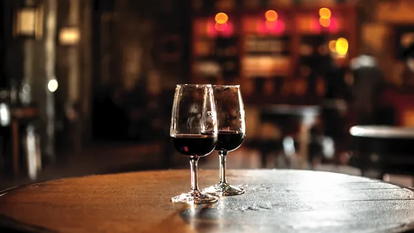 Dos copas de vino tinto sobre barrica en una bodega iluminada.