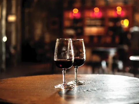 Dos copas de vino tinto sobre barrica en una bodega iluminada.