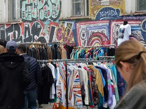 Gente revisando percheros de ropa con grafiti al fondo en Berlín.