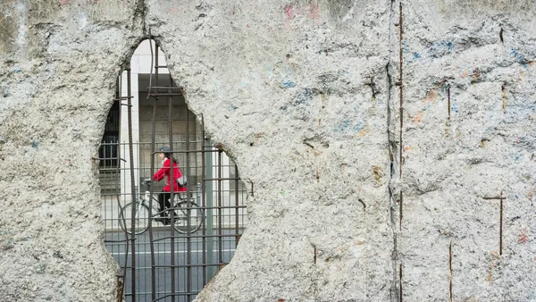 Persona en bicicleta vista a través de una grieta del Muro de Berlín con barras de acero