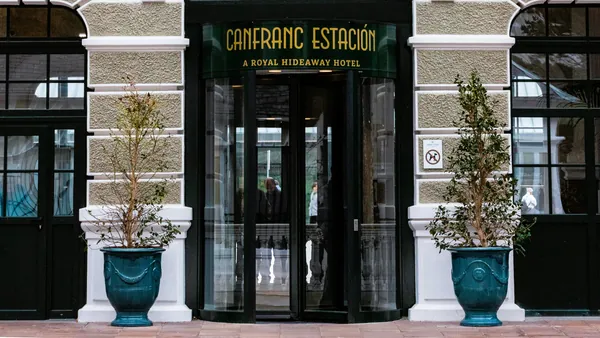 Entrada principal con puerta giratoria del Canfranc Estación, A Royal Hideaway Hotel, con maceteros flanqueando la puerta.
