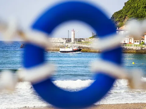 Barco pesquero en el mar enmarcado por un salvavidas azul en Llanes, Asturias.