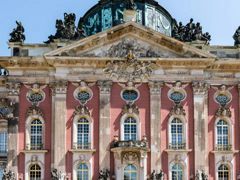 Fachada principal del Detalle de la fachada barroca del Nuevo Palacio (Neues Palais) en Potsdam, con ladrillo rojo, estatuas y cúpula.