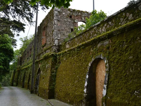 Muro cubierto de musgo y ruinas antiguas en un sendero forestal de la Quinta da Regaleira.