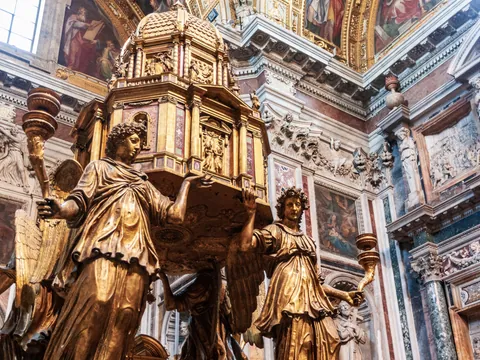 Escultura dorada de ángeles sosteniendo un relicario en un interior barroco de Roma