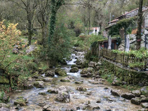 Río en Bulnes, Asturias, rodeado de casas de piedra, vegetación verde y un entorno natural de montaña.