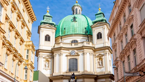 Fachada de la Iglesia de San Pedro en Viena, con su gran cúpula verde y torres barrocas iluminadas por el sol.