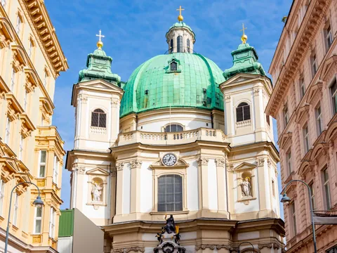 Fachada de la Iglesia de San Pedro en Viena, con su gran cúpula verde y torres barrocas iluminadas por el sol.
