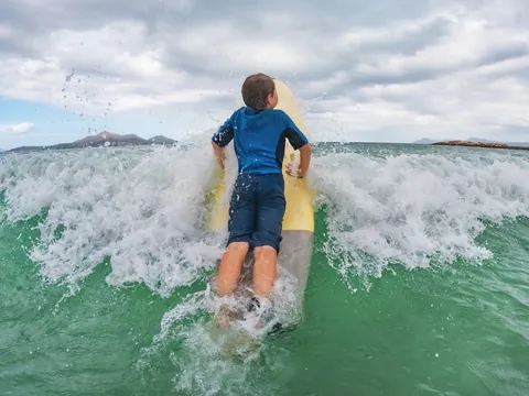 Niño sobre tabla de surf cruzando una ola en Mundaka, Vizcaya