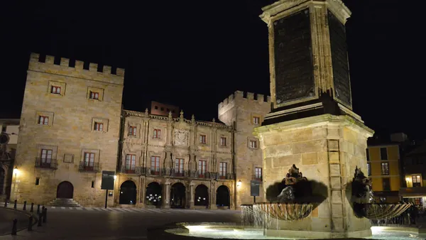 Vista nocturna del Palacio de Revillagigedo y la fuente del monumento a Pelayo iluminados en la plaza principal de Gijón