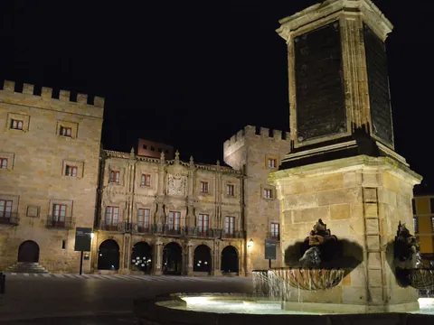Vista nocturna del Palacio de Revillagigedo y la fuente del monumento a Pelayo iluminados en la plaza principal de Gijón