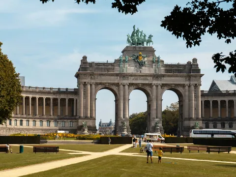 Arco del Triunfo en el Parque del Cincuentenario de Bruselas, con personas paseando y áreas verdes al frente.