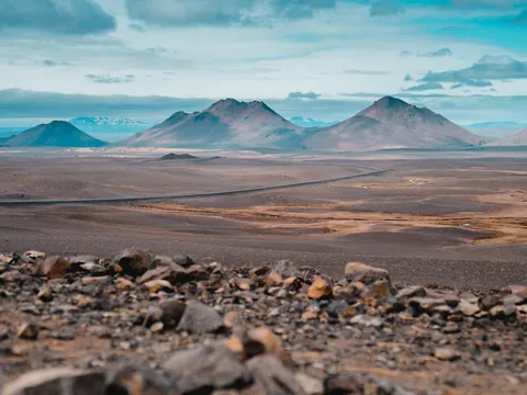 Paisaje volcánico cerca de Egilsstaðir, Islandia, con montañas y carretera entre terrenos áridos bajo cielo azul.