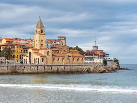 Iglesia de San Pedro Apóstol junto al mar en Gijón, con el casco antiguo y la playa de San Lorenzo al fondo