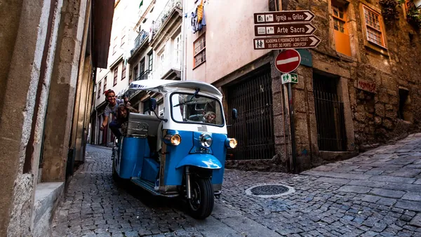 Tuk tuk azul recorriendo una calle estrecha empedrada en el casco histórico de Oporto.