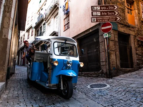 Tuk tuk azul recorriendo una calle estrecha empedrada en el casco histórico de Oporto.