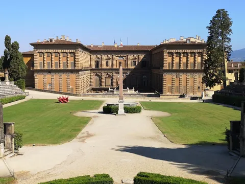 Vista frontal del Palacio Pitti en Florencia, Italia, con su arquitectura renacentista, amplio patio central, jardines simétricos y un obelisco en el centro.