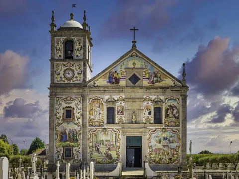 Fachada colorida de la Iglesia de Santa Maria de Válega en Portugal, cubierta con azulejos y campanario lateral.