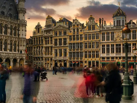 Personas paseando frente a edificios históricos con detalles dorados en la Grand Place de Bruselas al atardecer.