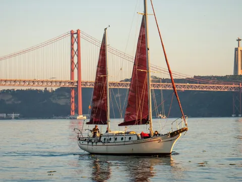 Velero navegando frente al Puente 25 de Abril y el Cristo Rei en Lisboa
