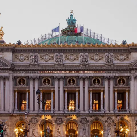 Fachada iluminada de la Ópera Garnier bajo el cielo del atardecer en París.