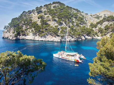 Catamarán navegando por las tranquilas aguas de la bahía de Alcudia, con vistas panorámicas al paisaje mediterráneo.