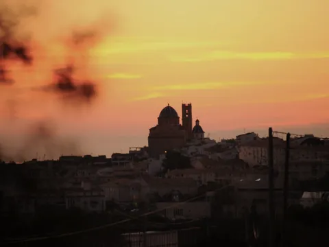 Silueta de la iglesia de Altea, con sus cúpulas azules, recortada contra un cielo de amanecer en tonos naranja y rojo.