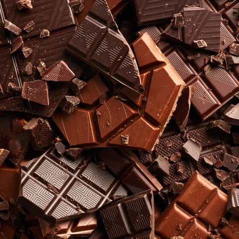Primer plano de tabletas y trozos de chocolate negro y con leche, de Astorga o artesanal, apilados en textura densa.