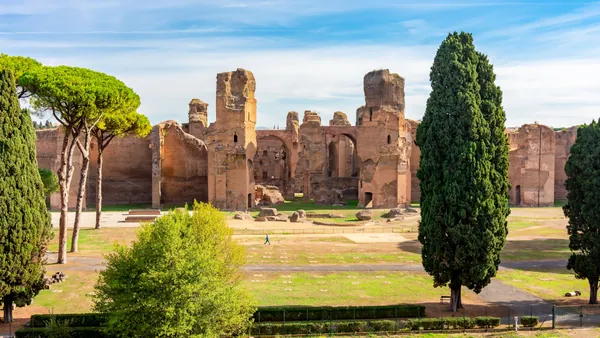 Ruinas de las Termas de Caracalla en Roma, antiguo complejo termal romano rodeado de cipreses y pinos bajo cielo azul.