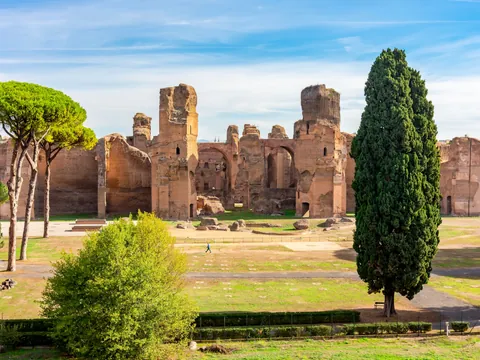 Ruinas de las Termas de Caracalla en Roma, antiguo complejo termal romano rodeado de cipreses y pinos bajo cielo azul.