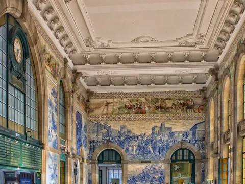 Interior de São Bento con murales de azulejos azules y gran reloj.