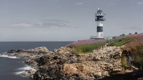 Faro de Isla Pancha en Ribadeo, sobre un acantilado cubierto de flores silvestres y con el mar Cantábrico al fondo.