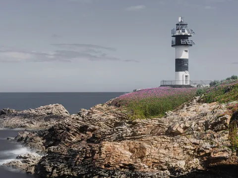 Faro de Isla Pancha en Ribadeo, sobre un acantilado cubierto de flores silvestres y con el mar Cantábrico al fondo.