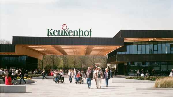 Entrada principal del parque Keukenhof en los Países Bajos, con varias personas caminando y disfrutando del lugar en un día soleado, y el letrero "Keukenhof" visible sobre la entrada.