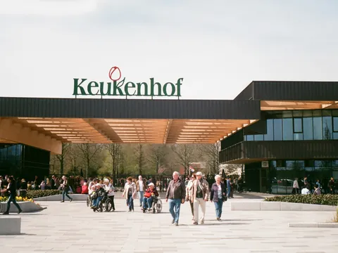 Entrada principal del parque Keukenhof en los Países Bajos, con varias personas caminando y disfrutando del lugar en un día soleado, y el letrero "Keukenhof" visible sobre la entrada.