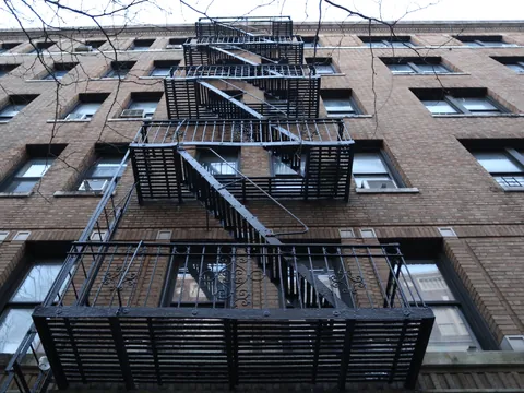 Contrapicado de un edificio de ladrillo en Nueva York con una escalera de incendios metálica y negra en la fachada.