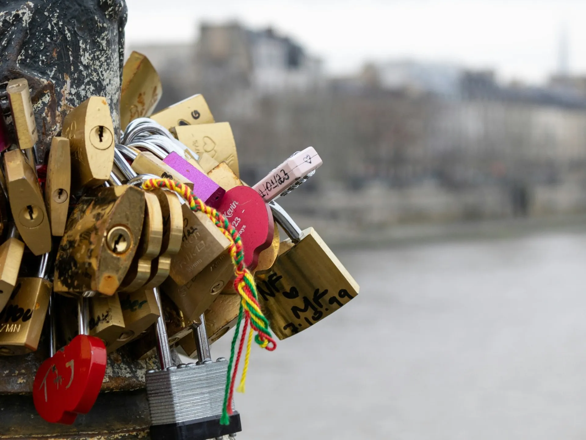 Candados de amor colgados en un poste junto al río Sena con París de fondo.