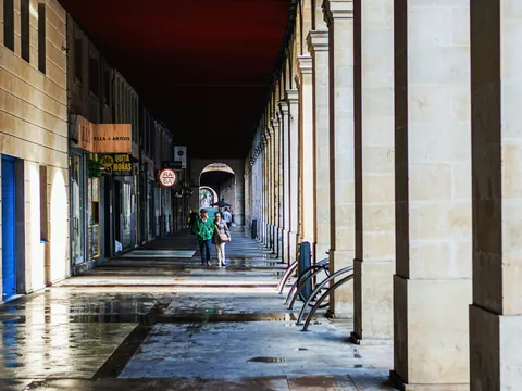 Pareja paseando bajo los soportales de piedra de la Plaza Mayor de Gijón.