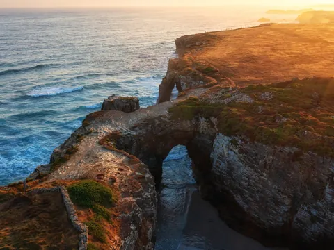 Vista aérea de la Playa de las Catedrales al atardecer, con sus arcos de roca bañados por el mar Cantábrico.