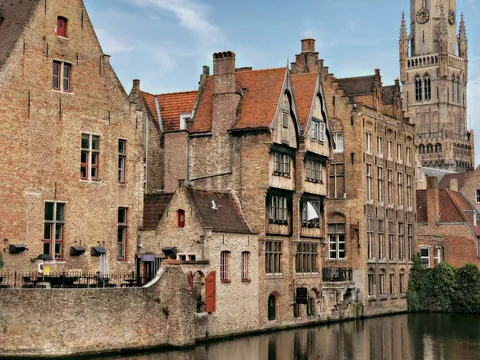 Casas medievales de ladrillo junto a un canal de Brujas, Bélgica, con el campanario.