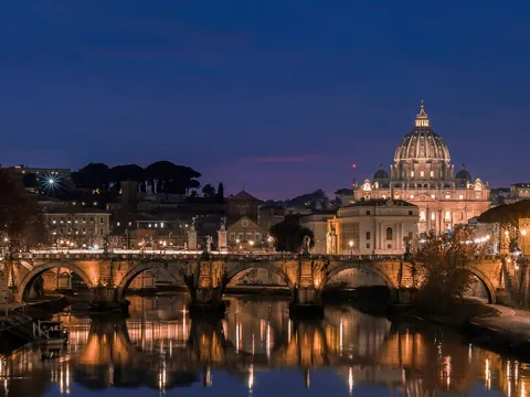 Basílica de San Pedro iluminada al anochecer con el río Tíber y el puente en Roma