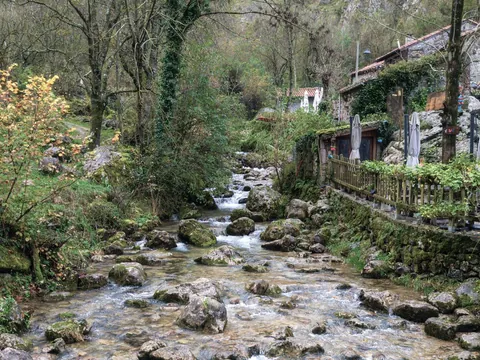 Río en Bulnes, Asturias, rodeado de casas de piedra, vegetación verde y un entorno natural de montaña.