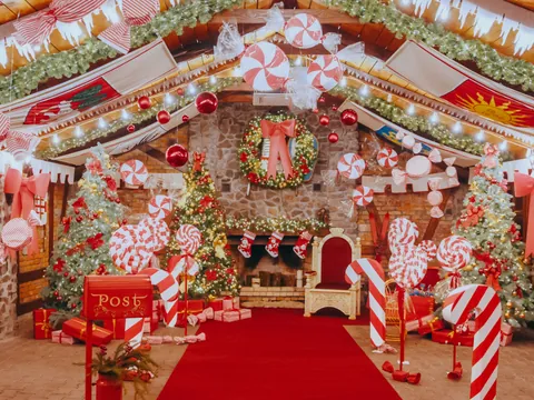 Decoración navideña en una sala con chimenea, árboles iluminados, guirnaldas, bastones de caramelo y adornos rojos, creando un ambiente festivo típico de la Navidad.