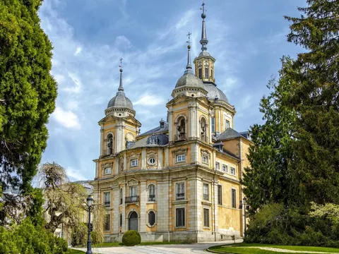 Colegiata del Palacio Real de La Granja de San Ildefonso entre árboles verdes.