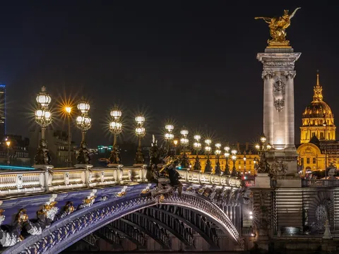 Puente Alejandro III iluminado de noche con Los Inválidos al fondo en París.