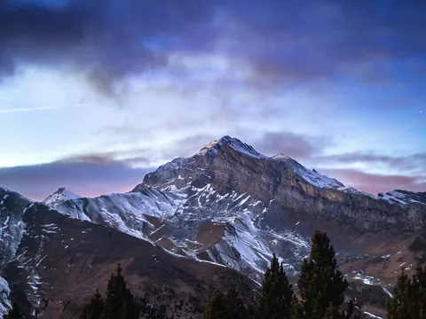 Paisaje nocturno de montaña nevada bajo un cielo estrellado y nublado en Aínsa.