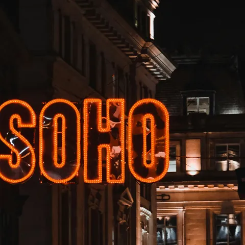 Letrero neón naranja con la palabra SOHO en una calle nocturna de Londres.