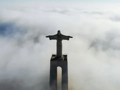 Cristo Rei emergiendo entre nubes sobre Lisboa en una vista aérea
